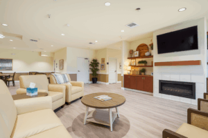 Community lounge at Valley Spring Memory Care with comfortable seating, fireplace, TV, and warm decor for residents and visitors to relax.